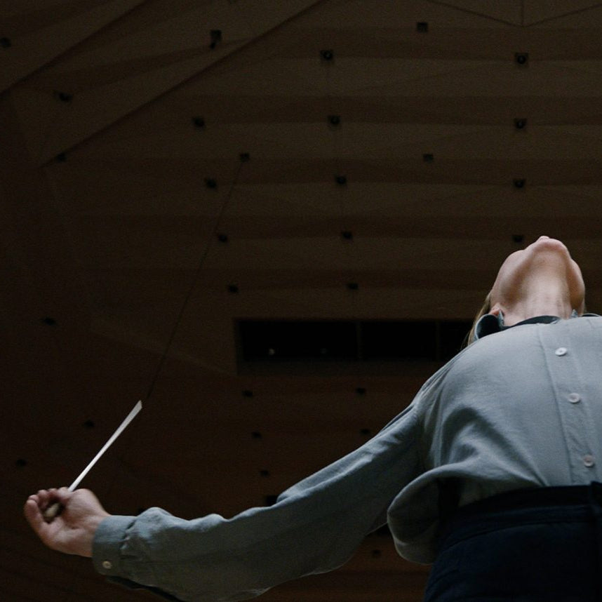 Low shot of Lydia Tar with hands and head raised conducting an unseen orchestra.